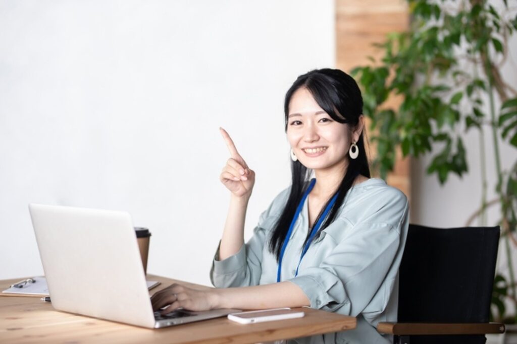 ノートPCの前で指を立てて笑う女性